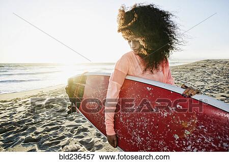 Stock Photo - Hispanic woman holding surfboard at beach. Fotosearch