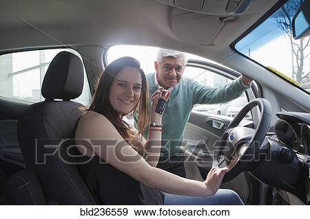 Stock Photo - Hispanic woman sitting in new car showing key. Fotosearch
