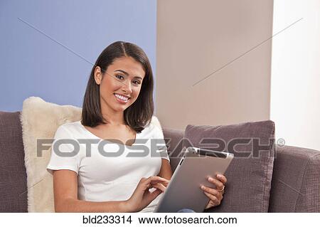 Hispanic woman sitting on sofa using digital tablet View Large Photo Image Picture - Hispanic woman sitting on sofa using digital tablet. Fotosearch