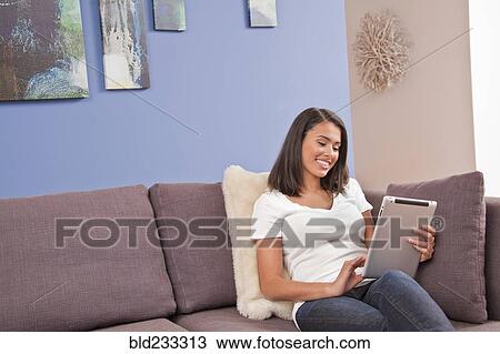 Hispanic woman sitting on sofa using digital tablet View Large Photo Image Stock Image - Hispanic woman sitting on sofa using digital tablet. Fotosearch