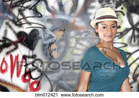 Stock Image - Hispanic woman standing near graffitied wall. Fotosearch