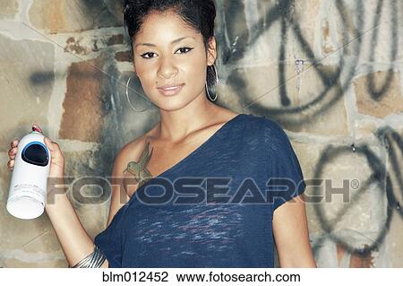 Stock Image - Hispanic woman tagging wall with graffiti. Fotosearch