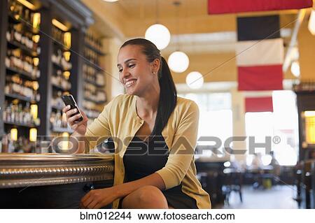 Picture - Hispanic woman using cell phone in restaurant bar. Fotosearch