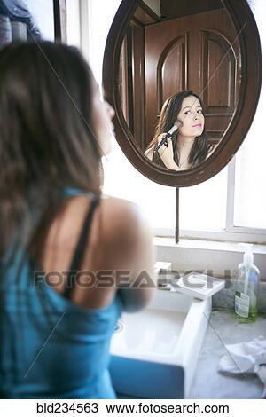 Stock Image - Hispanic woman using makeup brush in mirror. Fotosearch
