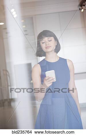 Hispanic woman wearing blue dress texting on cell phone behind window View Large Photo Image Picture - Hispanic woman wearing blue dress texting on cell phone behind window. Fotosearch