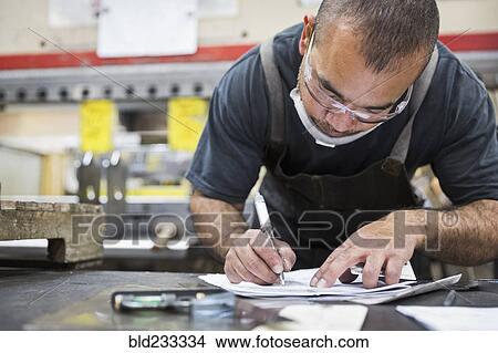 Hispanic worker writing on paperwork in factory View Large Photo Image Picture - Hispanic worker writing on paperwork in factory. Fotosearch