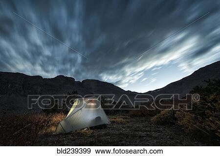 Stock Photo - Illuminated camping tent under cloudy sky. Fotosearch
