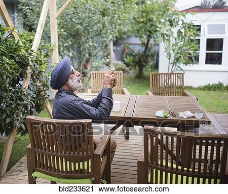 Stock Image - Indian man photographing with cell phone on backyard patio. Fotosearch