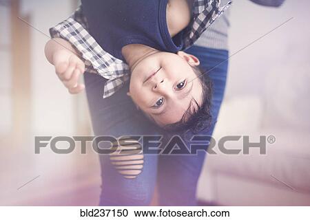 Stock Image - Indian mother holding baby son upside-down. Fotosearch