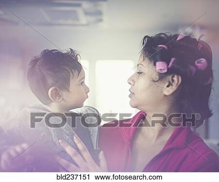 Stock Image - Indian mother wearing curlers holding son. Fotosearch
