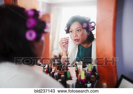 Stock Image - Indian woman wearing curlers applying makeup. Fotosearch