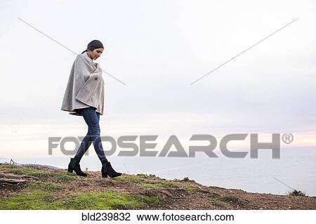 Stock Image - Indian woman wearing poncho walking on hill. Fotosearch