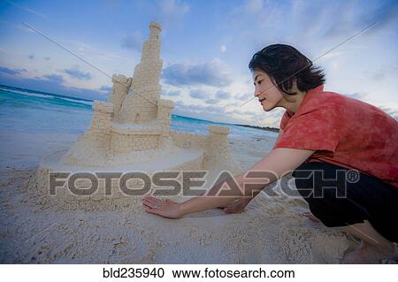 Stock Image - Japanese woman building elaborate sand castle at beach. Fotosearch