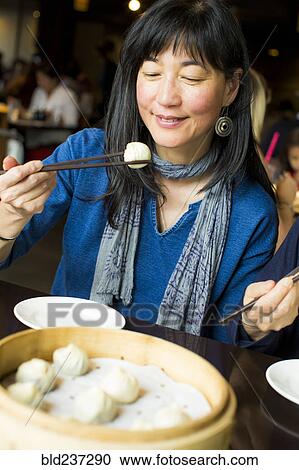Stock Image - Japanese woman eating food with chopsticks. Fotosearch