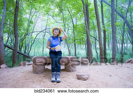 Stock Image - Japanese woman sitting on bench at park. Fotosearch