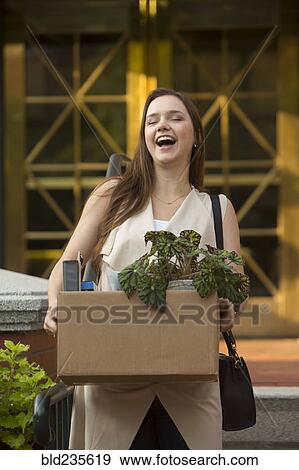 Stock Photo - Laughing Caucasian carrying box with potted plant. Fotosearch