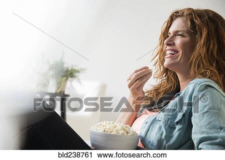 Stock Image - Laughing Caucasian woman eating bowl of popcorn. Fotosearch