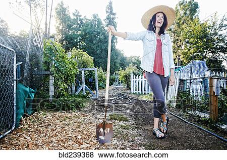 Stock Photo - Laughing Caucasian woman leaning on shovel in garden. Fotosearch
