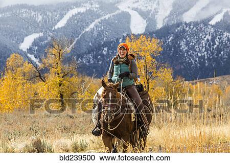 Stock Image - Laughing Caucasian woman riding horse in winter. Fotosearch