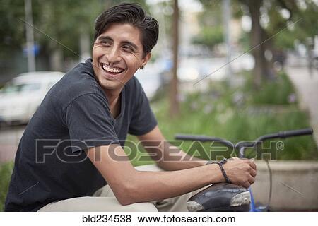 Stock Photo - Laughing Hispanic man sitting with bicycle. Fotosearch