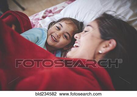 Laughing Hispanic mother and daughter under red blanket in bed View Large Photo Image Stock Image - Laughing Hispanic mother and daughter under red blanket in bed. Fotosearch