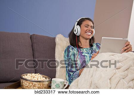 Laughing Hispanic woman sitting on sofa with digital tablet View Large Photo Image Stock Photo - Laughing Hispanic woman sitting on sofa with digital tablet. Fotosearch