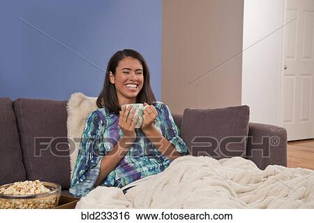 Laughing Hispanic woman sitting on sofa drinking warm beverage View Large Photo Image Stock Photograph - Laughing Hispanic woman sitting on sofa drinking warm beverage. Fotosearch