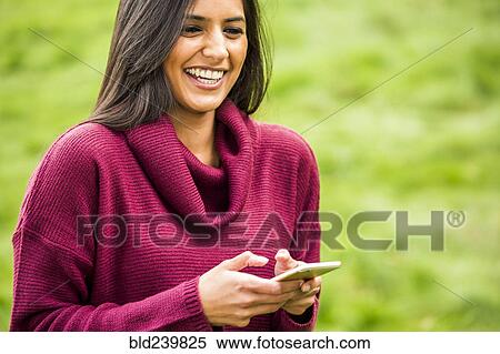Stock Photography - Laughing Indian woman texting on cell phone. Fotosearch