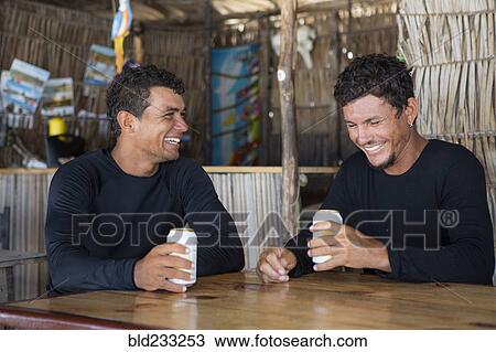 Stock Image - Laughing men holding beverage cans in bar. Fotosearch