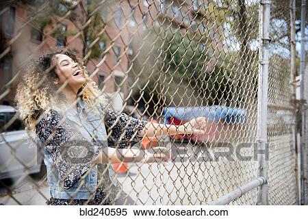 Laughing Mixed Race woman holding chain-link fence in city View Large Photo Image Stock Photography - Laughing Mixed Race woman holding chain-link fence in city. Fotosearch