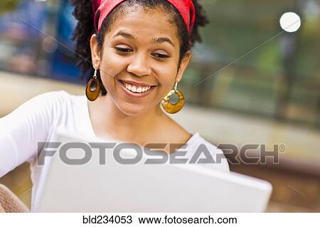 Stock Image - Laughing Mixed Race woman using laptop. Fotosearch
