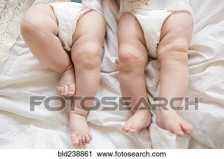 Stock Image - Legs of Caucasian twin baby girls laying on bed. Fotosearch