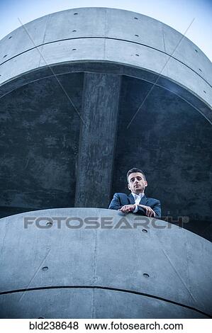 Stock Photo - Low angle view of businessman leaning on balcony. Fotosearch