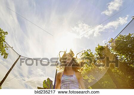 Stock Photo - Low angle view of Caucasian girl jumping on trampoline. Fotosearch