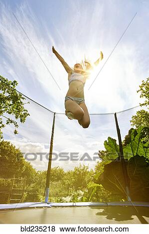 Stock Photo - Low angle view of Caucasian girl jumping on trampoline. Fotosearch