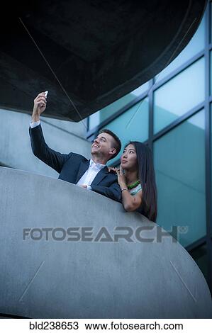 Low angle view of couple on balcony posing for cell phone selfie View Large Photo Image Stock Image - Low angle view of couple on balcony posing for cell phone selfie. Fotosearch