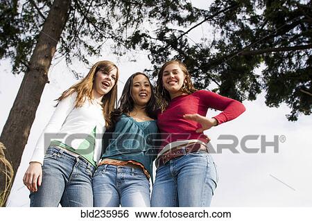 Stock Photograph - Low angle view of smiling girls near tree. Fotosearch
