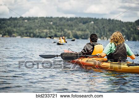 Stock Image - Man and woman holding paddles in kayak. Fotosearch