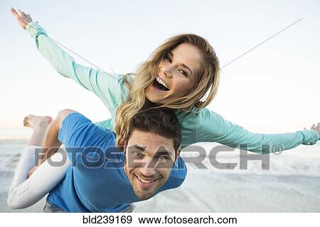 Stock Photo - Man carrying woman piggyback at beach. Fotosearch