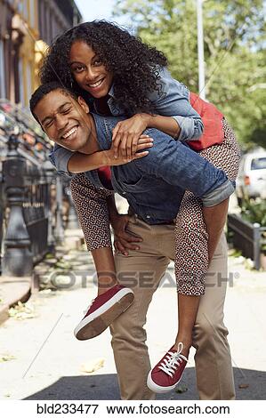Stock Photo - Man carrying woman piggyback on city sidewalk. Fotosearch