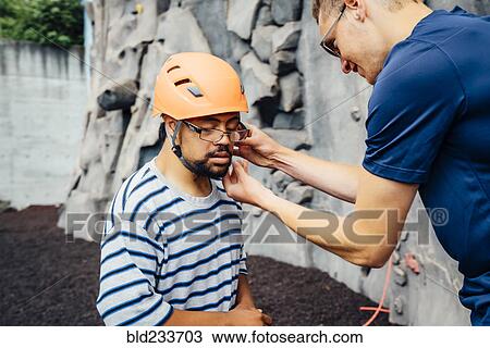 Stock Image - Man helping rock climber fasten helmet. Fotosearch