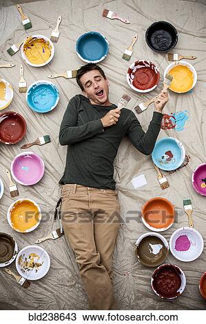Man laying on tarp holding paintbrushes and singing View Large Photo Image Stock Image - Man laying on tarp holding paintbrushes and singing. Fotosearch
