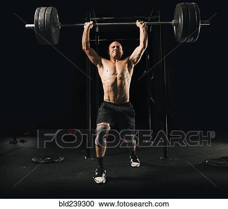 Man lifting heavy barbell in gymnasium View Large Photo Image Stock Image - Man lifting heavy barbell in gymnasium. Fotosearch
