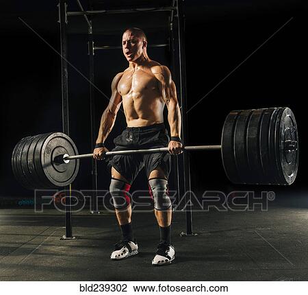 Man lifting heavy barbell in gymnasium View Large Photo Image Stock Image - Man lifting heavy barbell in gymnasium. Fotosearch