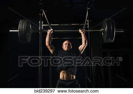 Man lifting heavy barbell in gymnasium View Large Photo Image Stock Photo - Man lifting heavy barbell in gymnasium. Fotosearch