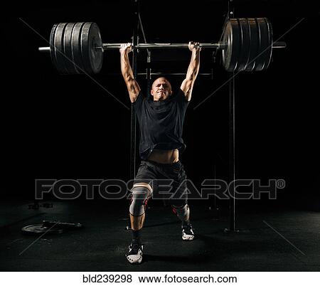 Stock Photo - Man lifting heavy barbell in gymnasium. Fotosearch