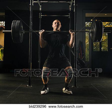 Man lifting heavy barbell in gymnasium View Large Photo Image Stock Photograph - Man lifting heavy barbell in gymnasium. Fotosearch