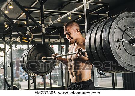 Man lifting heavy barbell in gymnasium View Large Photo Image Stock Photography - Man lifting heavy barbell in gymnasium. Fotosearch