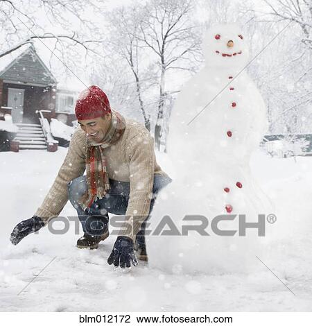 Stock Image - Man making snowman in front yard. Fotosearch
