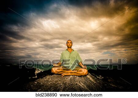Man meditating on rock near ocean under clouds View Large Photo Image Stock Image - Man meditating on rock near ocean under clouds. Fotosearch